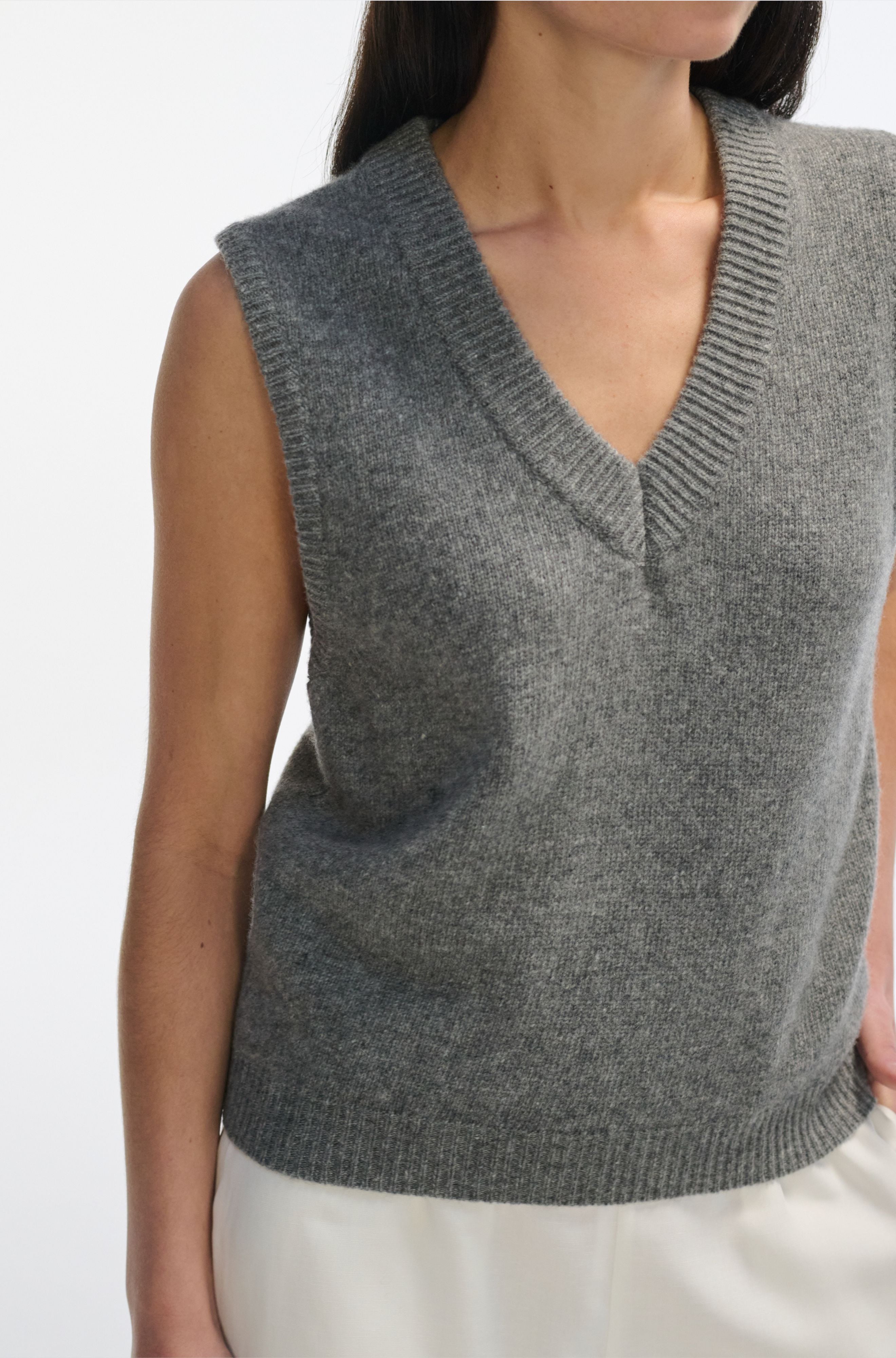 Gray knitted vest worn by a person on a white background