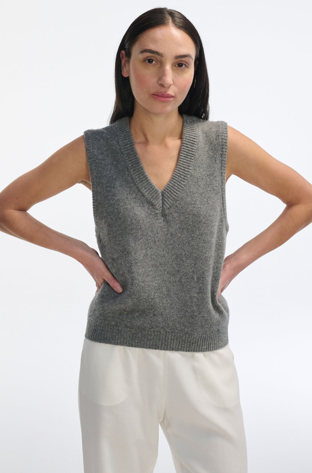 Woman wearing a gray knitted vest and white pants on a white background