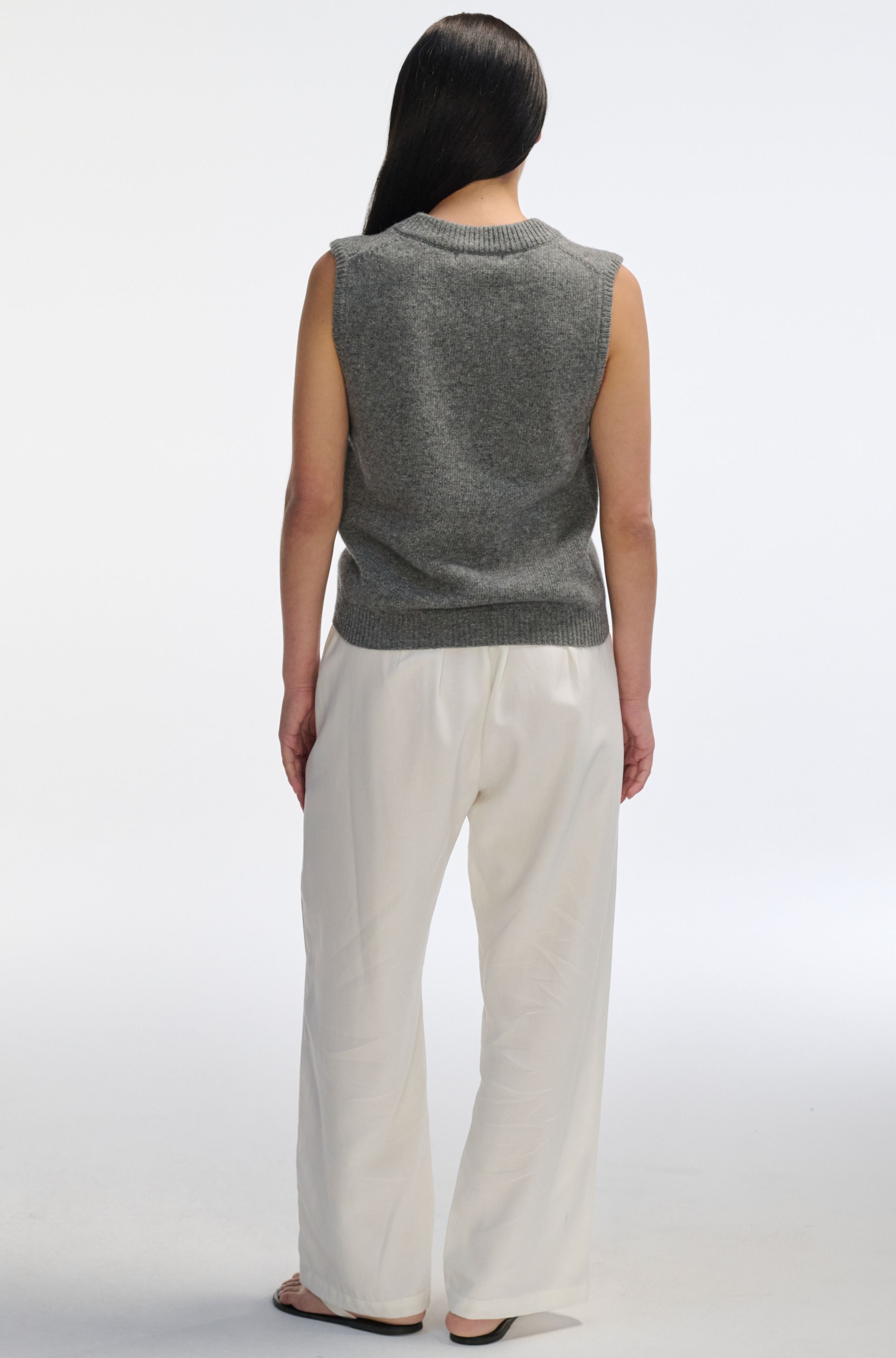 Person wearing a gray sleeveless sweater and white pants on a white background