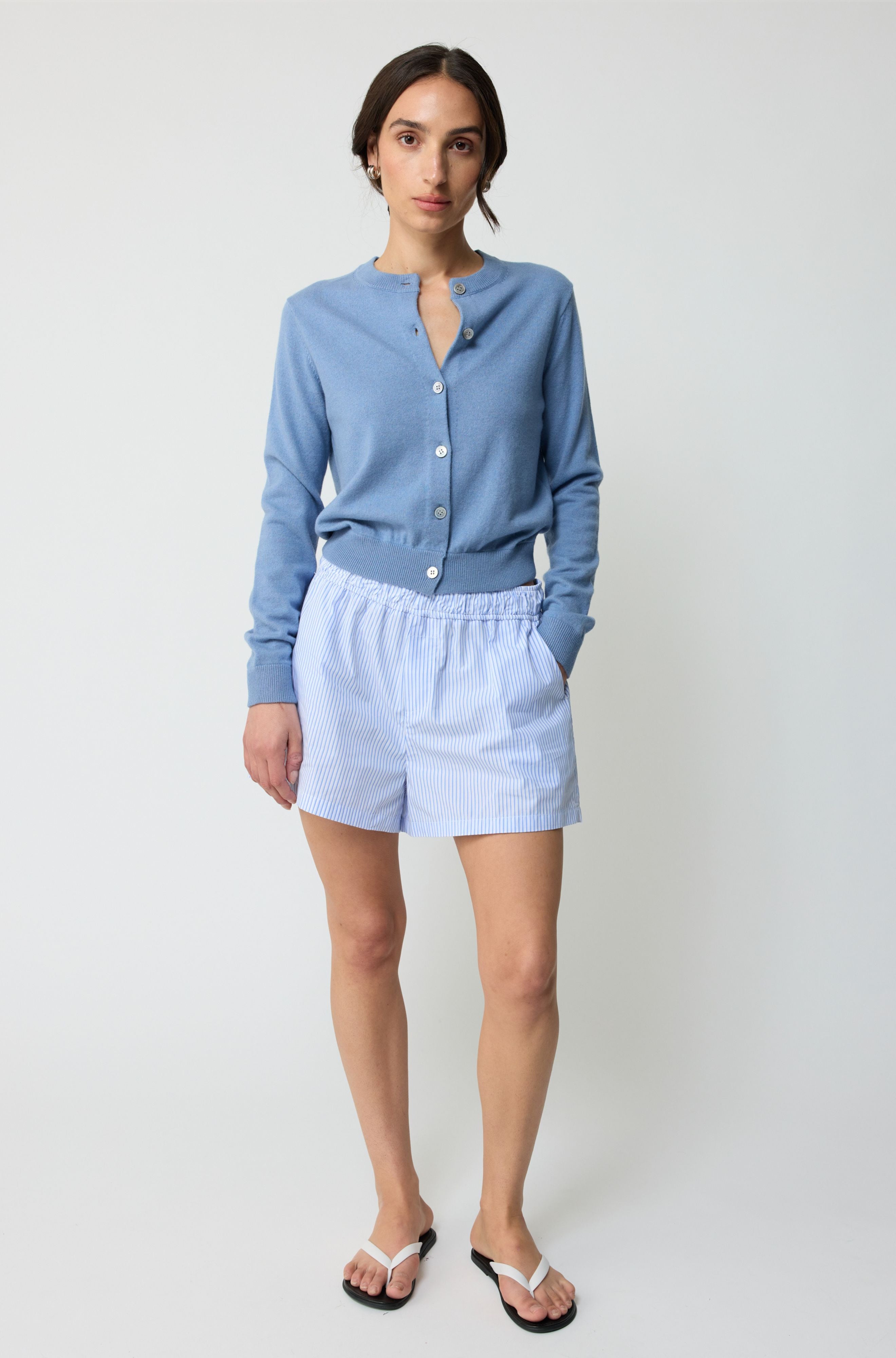 Woman wearing a light blue cardigan and shorts on a white background