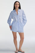 Woman wearing a light blue striped shirt and shorts on a white background