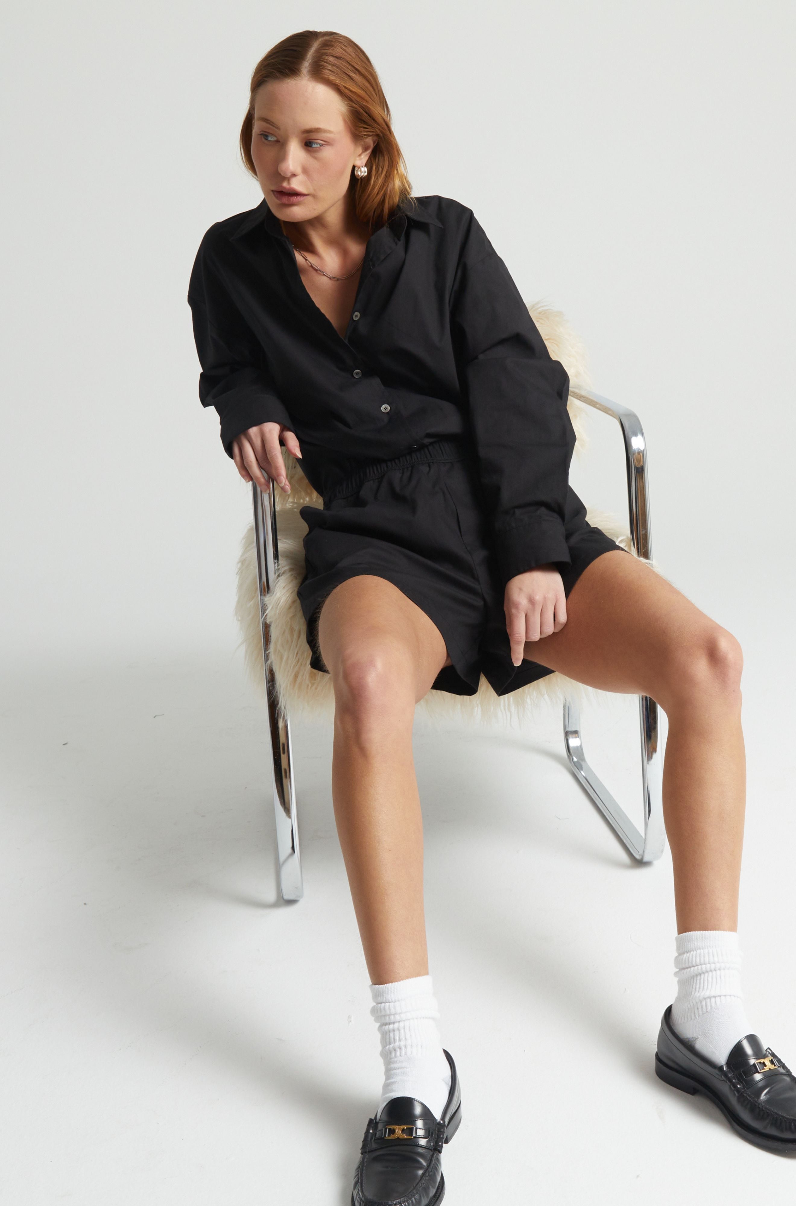 Woman sitting on a chair wearing a black outfit with white socks and black shoes.