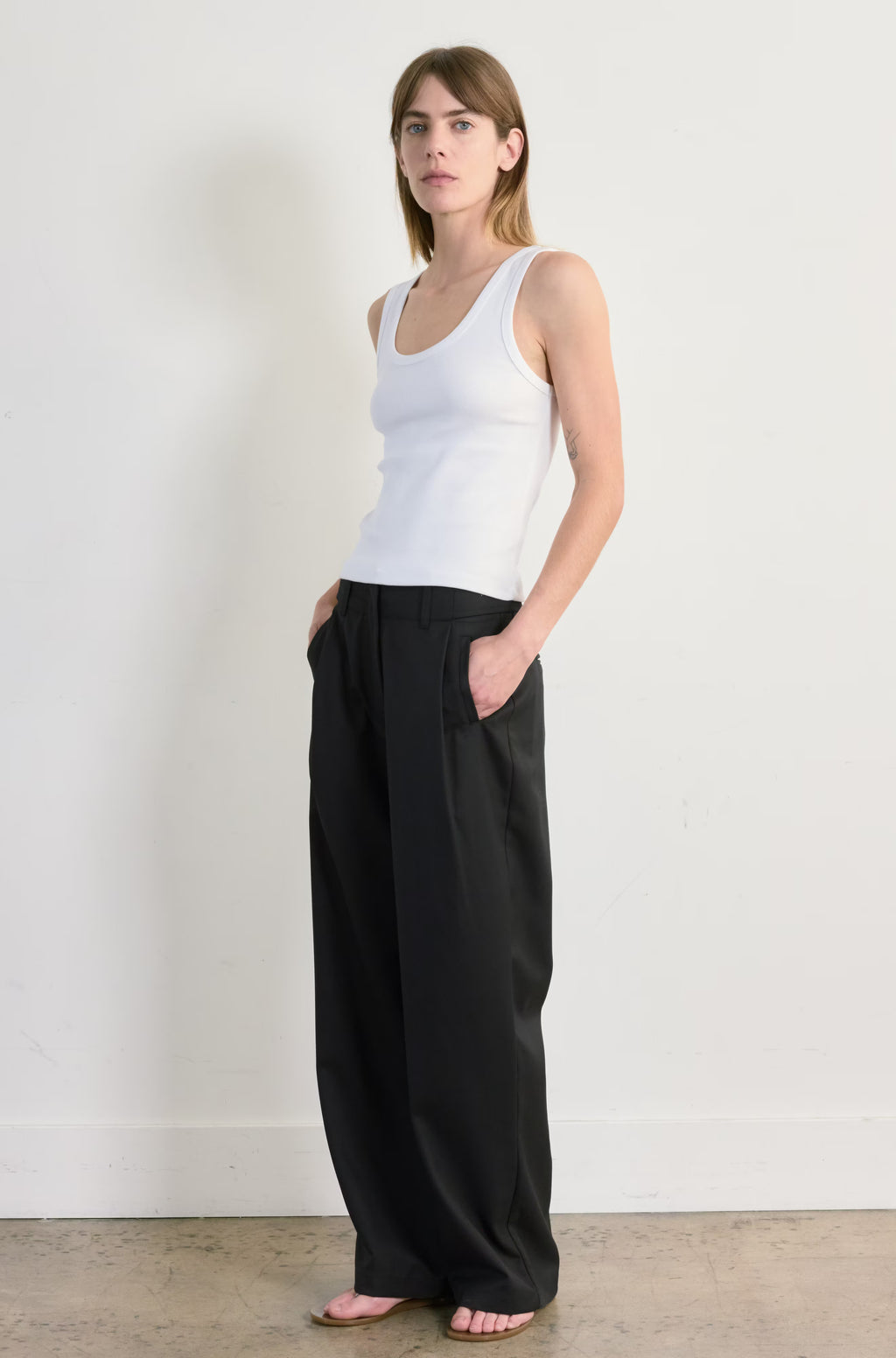 Woman wearing a white tank top and black pants against a plain background