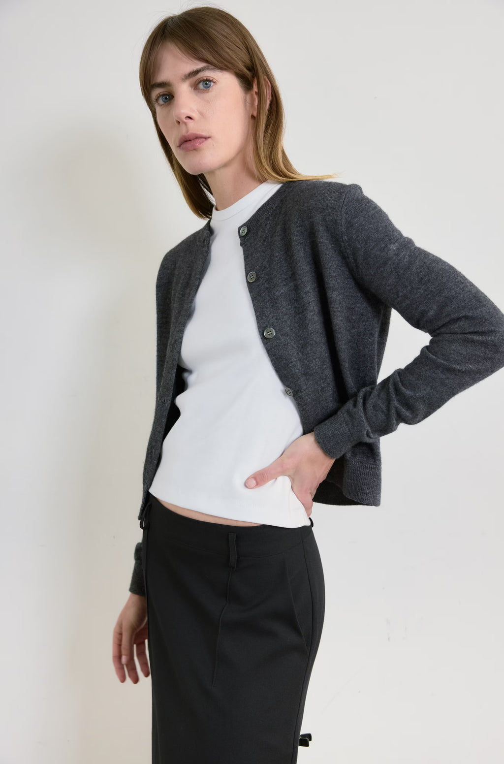 Woman wearing a gray cardigan over a white shirt and black skirt on a plain background