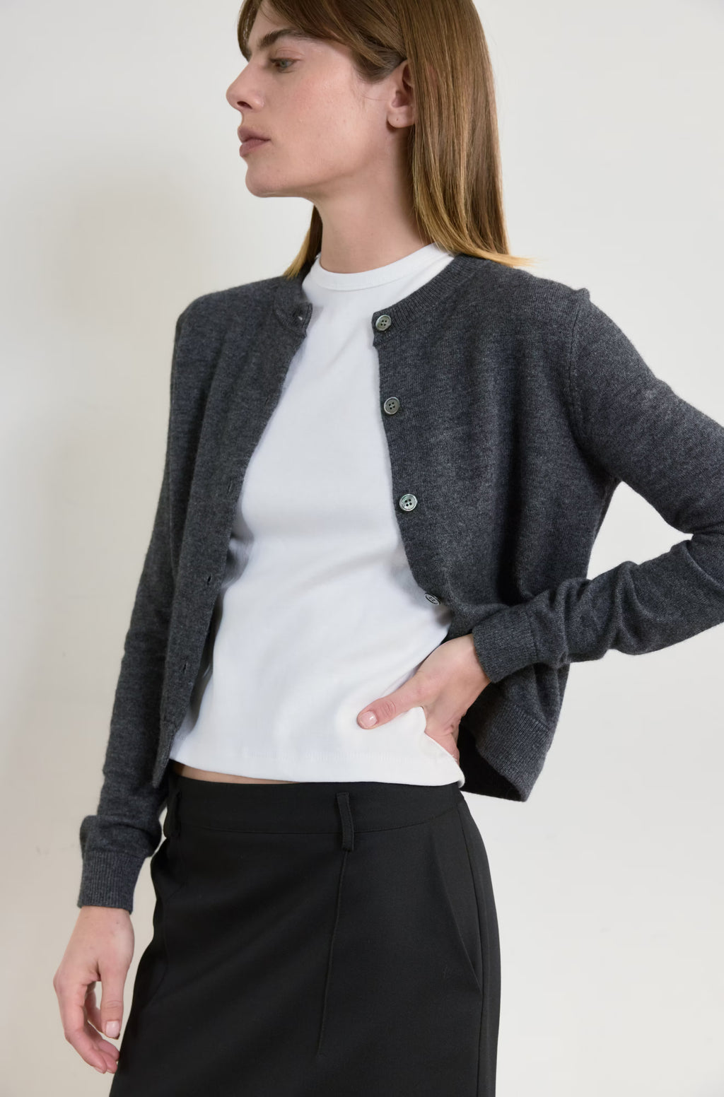 Woman wearing a gray cardigan over a white shirt with a plain background