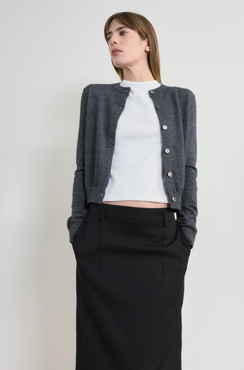Woman wearing a gray cardigan over a white shirt and black skirt on a plain background