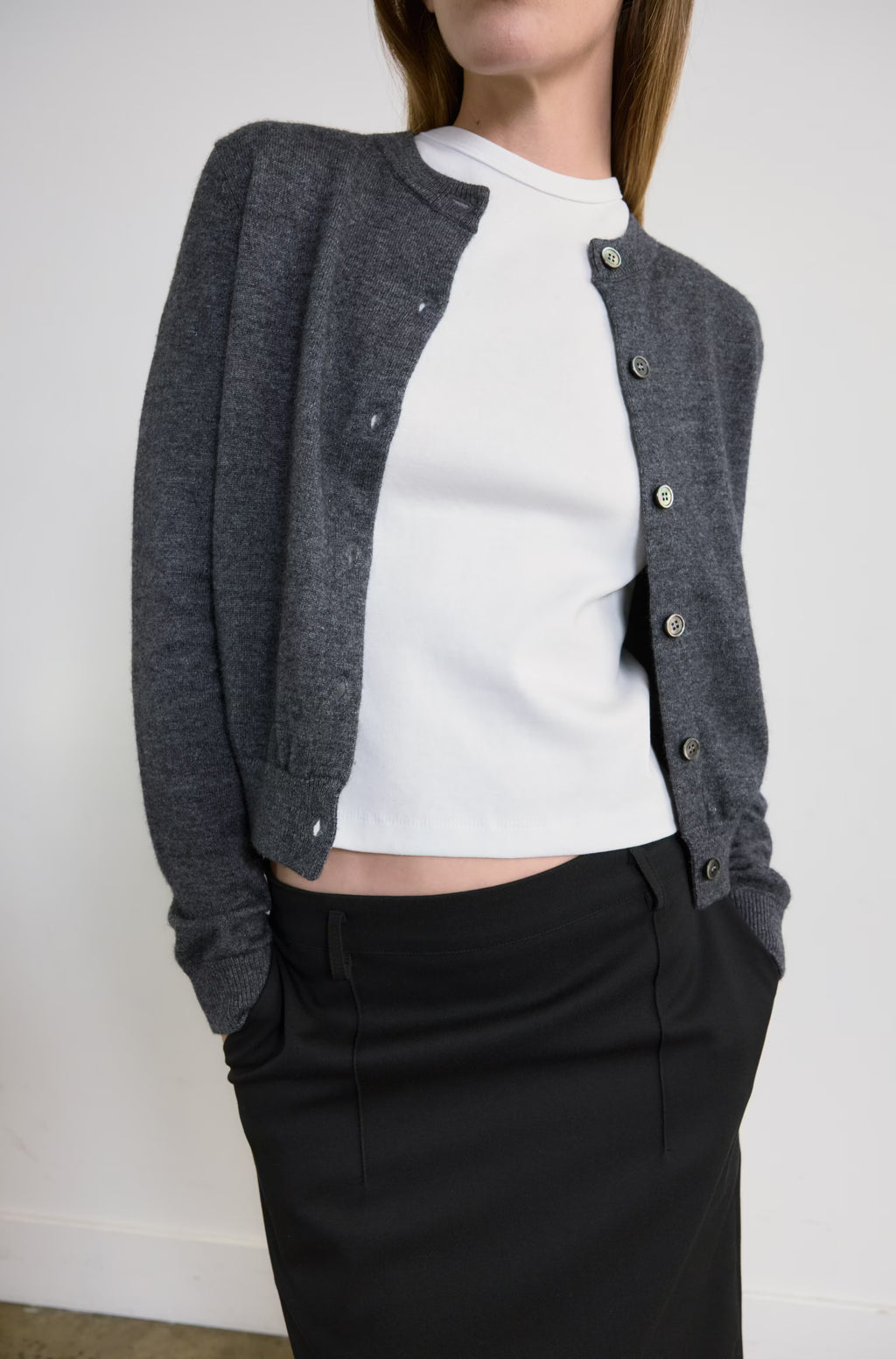 Person wearing a gray cardigan over a white shirt and black skirt against a plain background