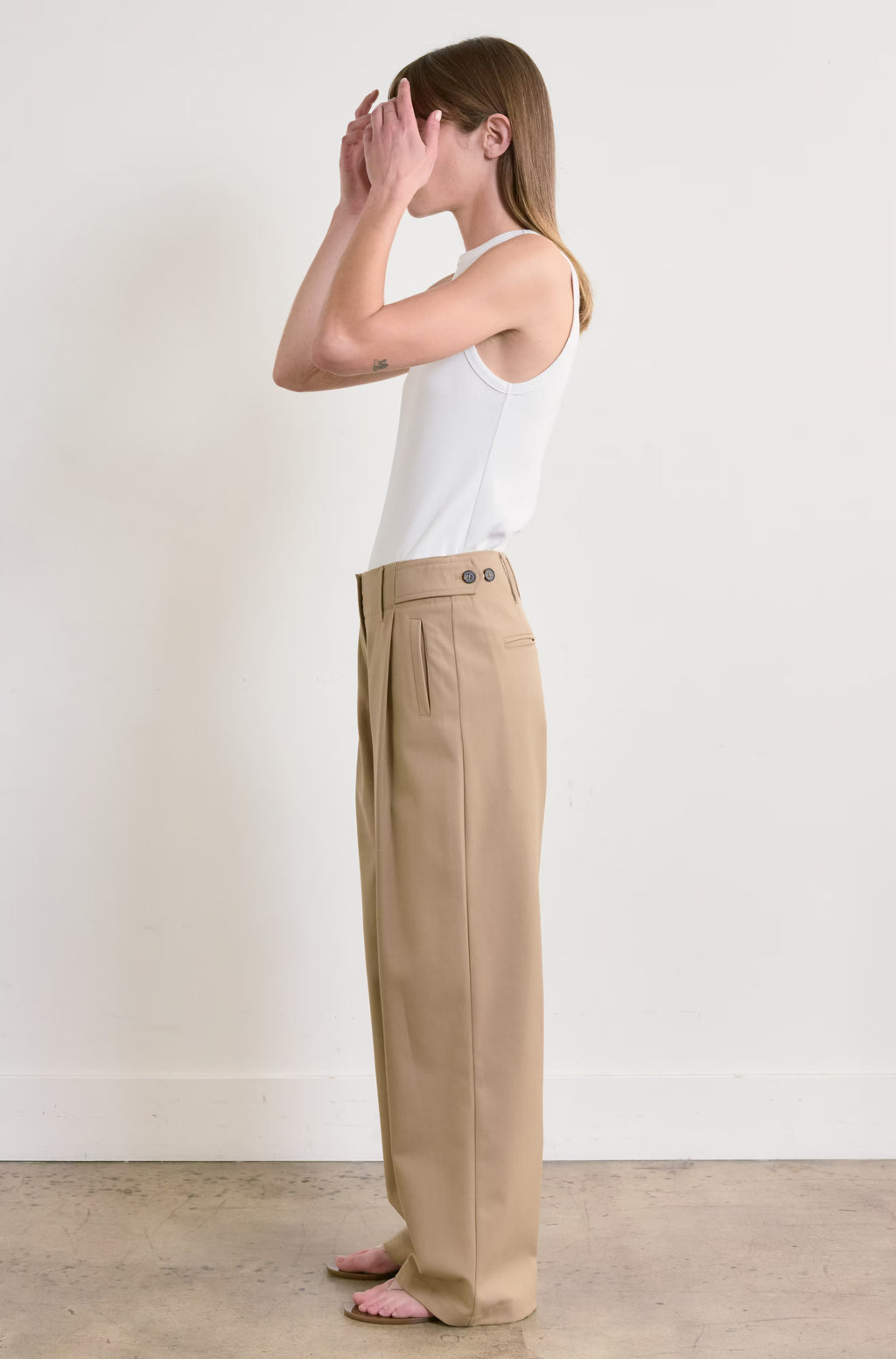 Person wearing beige pants and a white tank top against a plain background