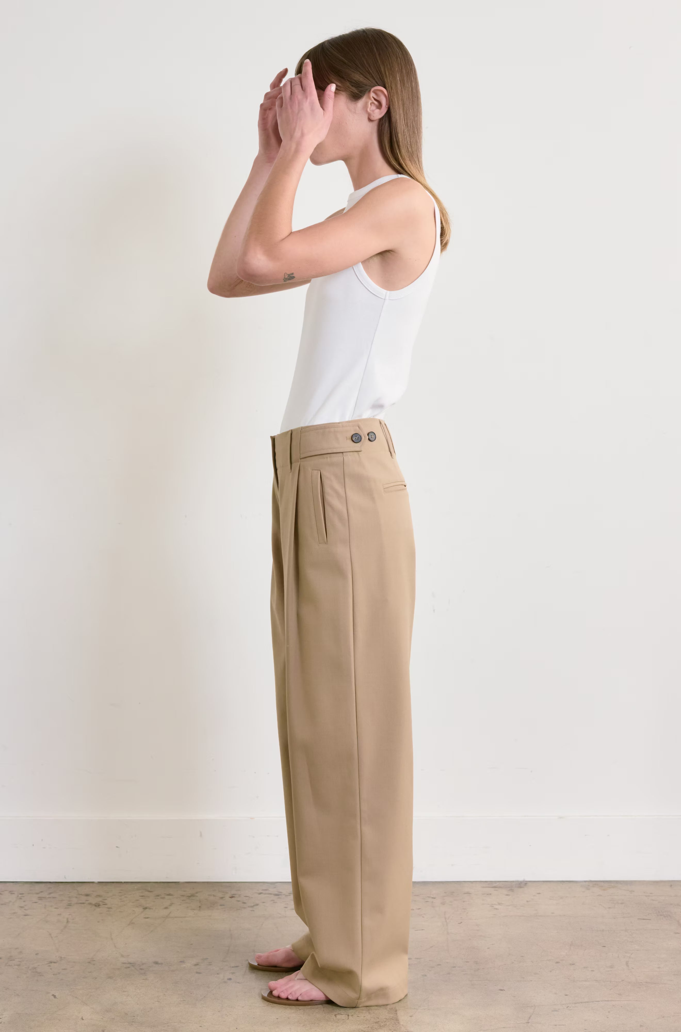 Person wearing beige pants and a white tank top against a plain background