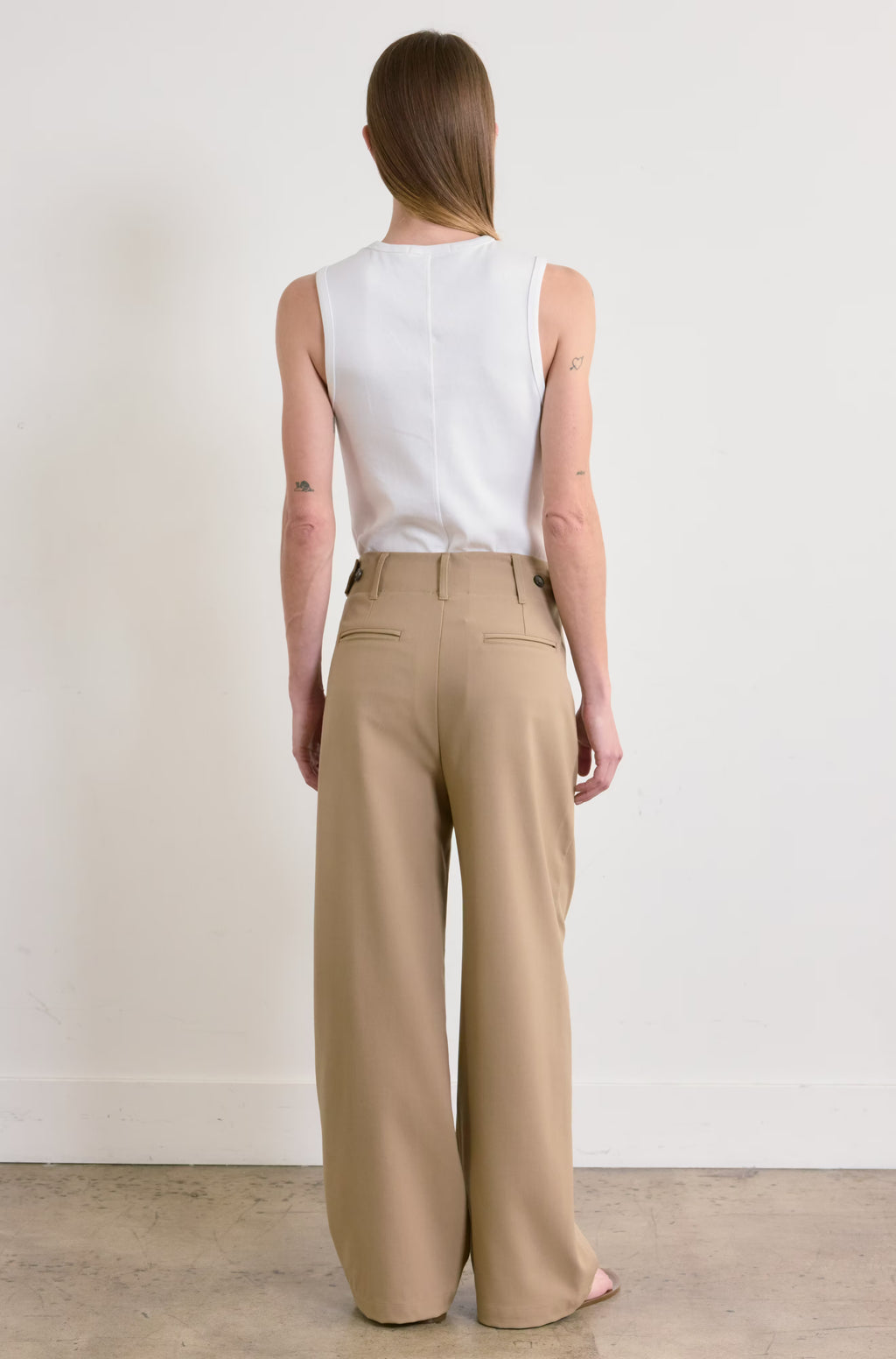 Person wearing a white sleeveless top and beige wide-leg pants against a plain background
