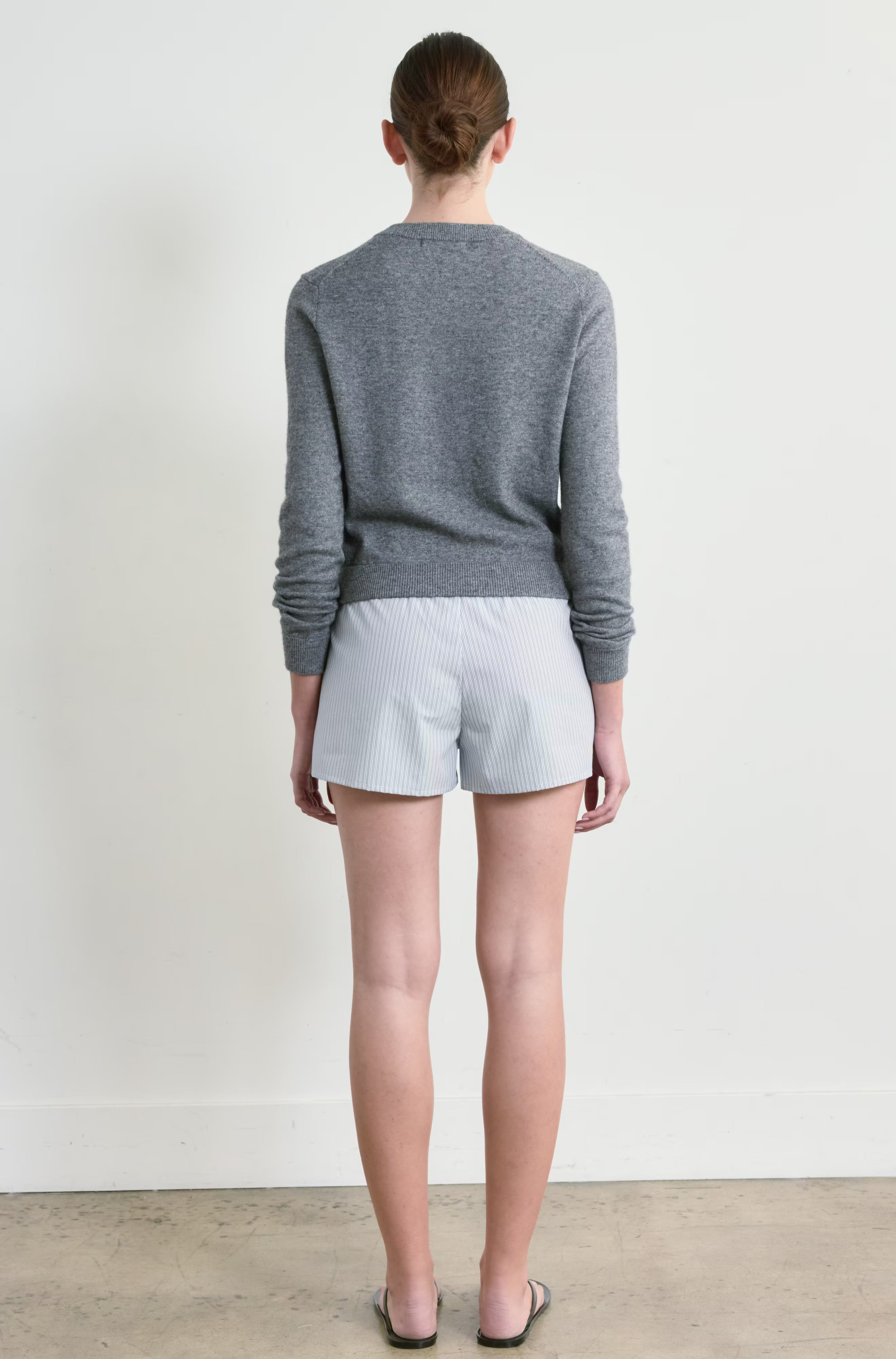 Person wearing a gray sweater and light gray stripe shorts against a white background
