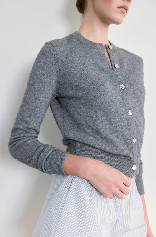 Person wearing a gray cardigan with button details against a white background