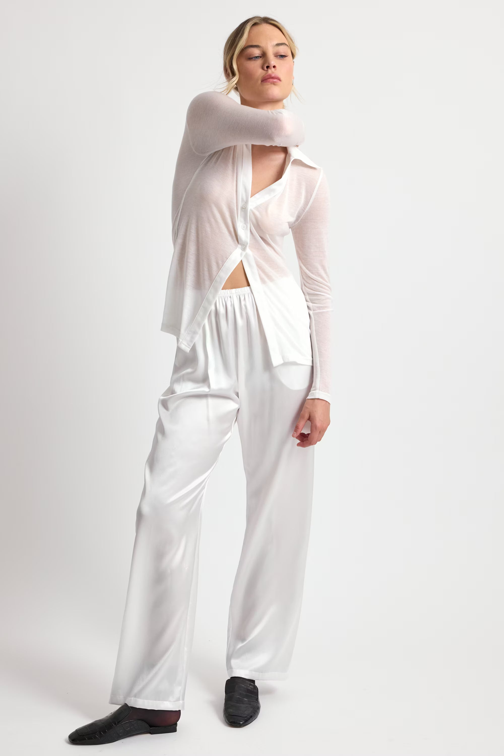 Woman wearing a white outfit with a cut-out design on a plain background