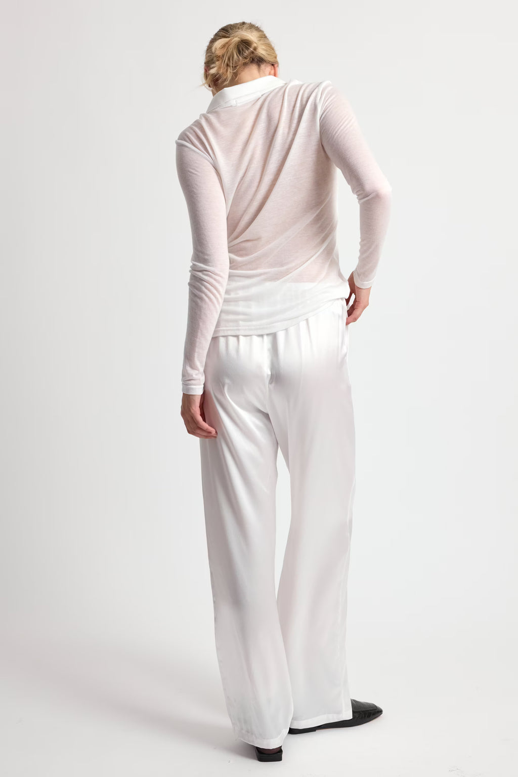 Person wearing a light pink long-sleeve top and white pants on a white background