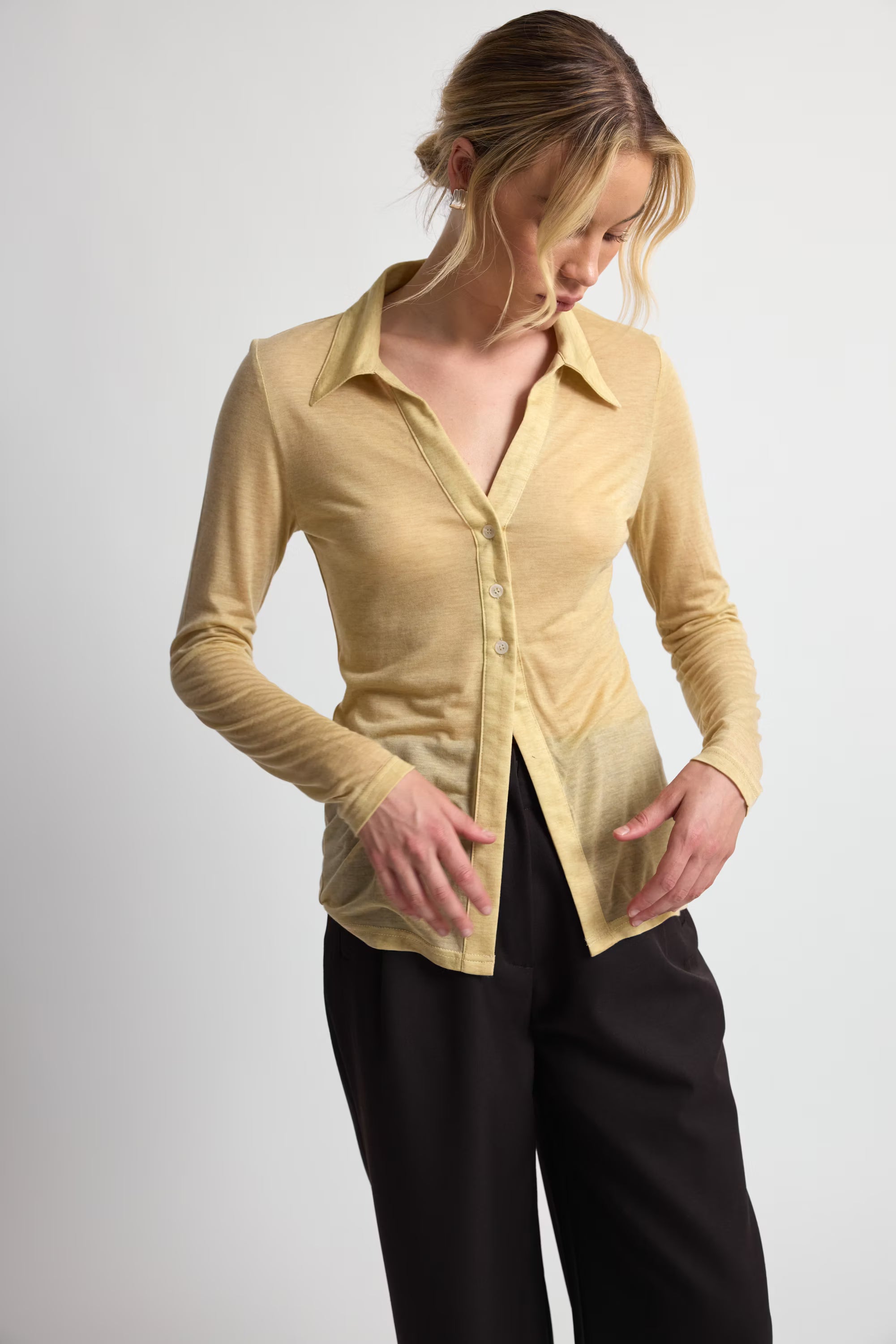 Woman wearing a yellow button-up shirt and black pants on a white background