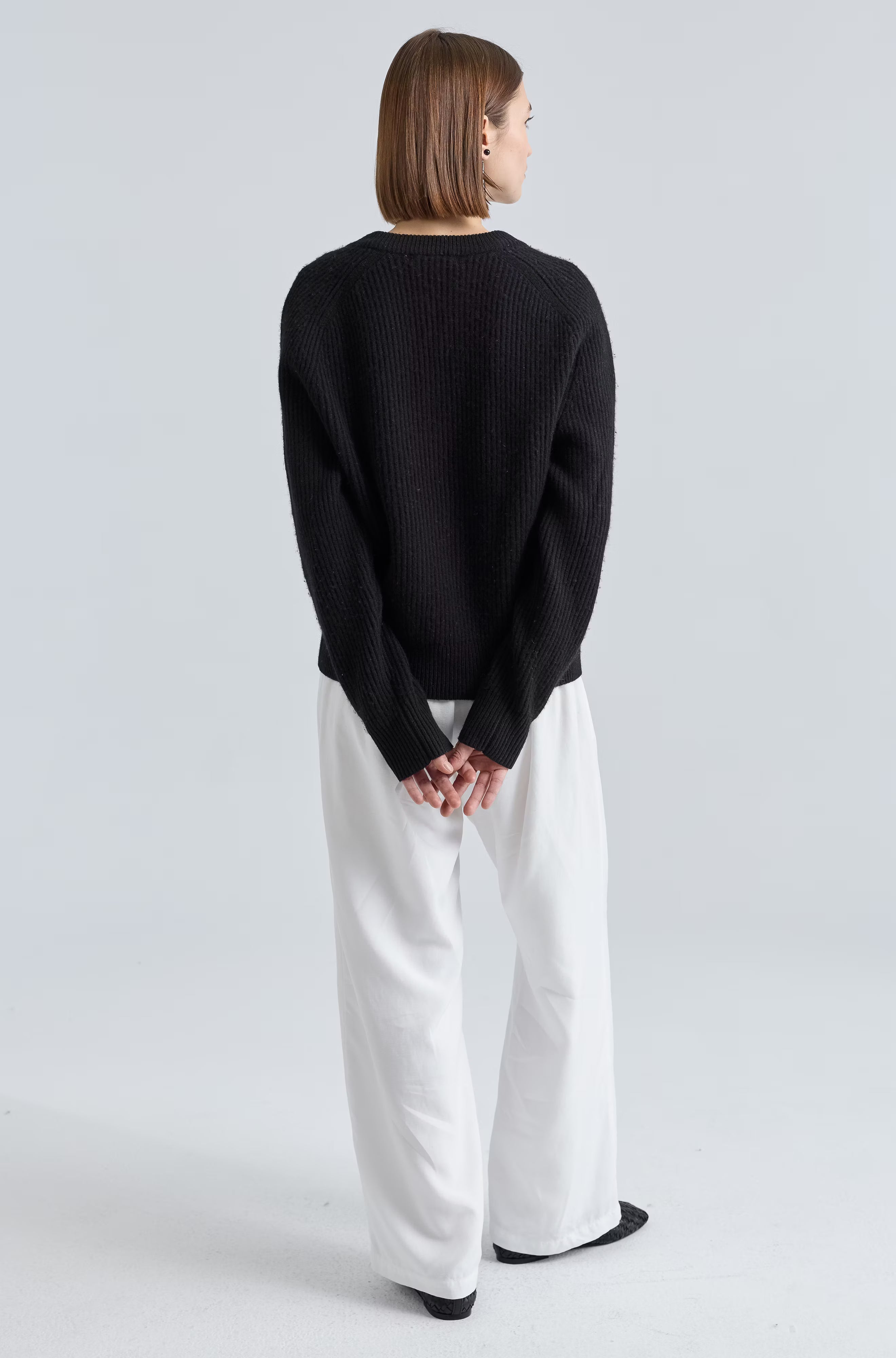 Person wearing a black sweater and white pants on a light gray background