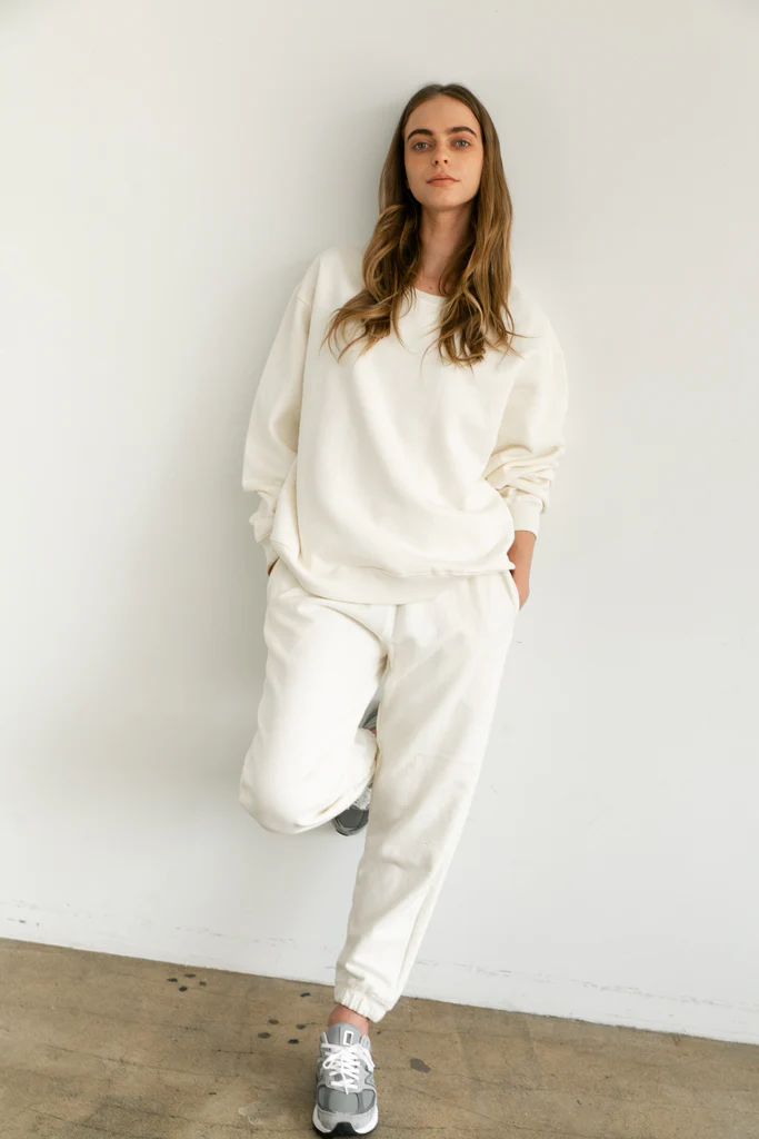 Woman wearing a white sweatsuit outfit against a plain white wall