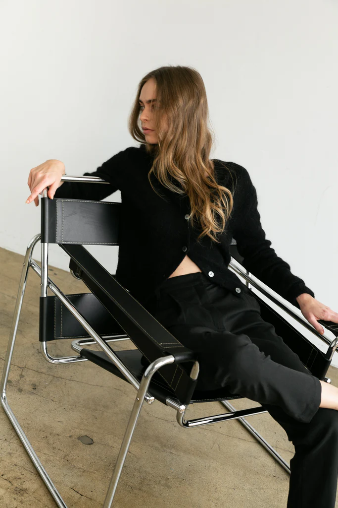 Woman sitting on a modern black and chrome chair against a white wall.