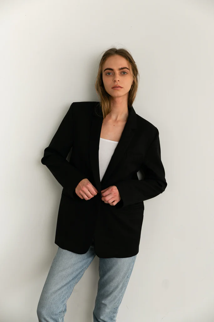 Woman wearing a black blazer over a white top and light blue jeans against a white background