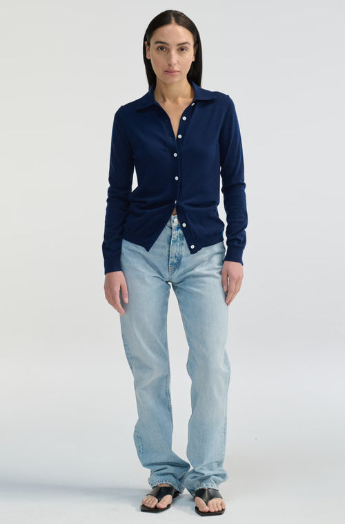 Woman wearing a navy blue button-up shirt and light blue jeans on a white background