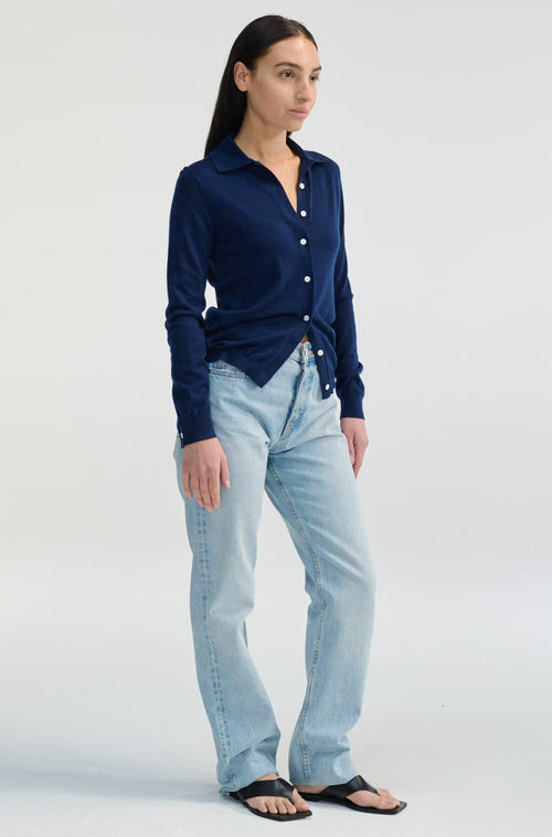 Woman wearing a navy blue cardigan and light blue jeans on a white background