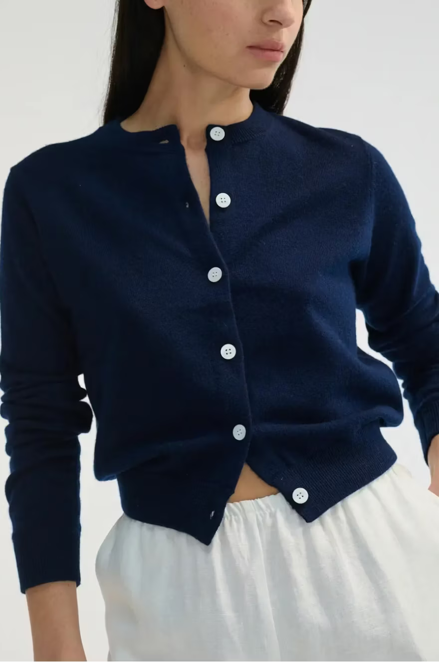 Woman wearing a navy blue cardigan with white buttons on a plain background