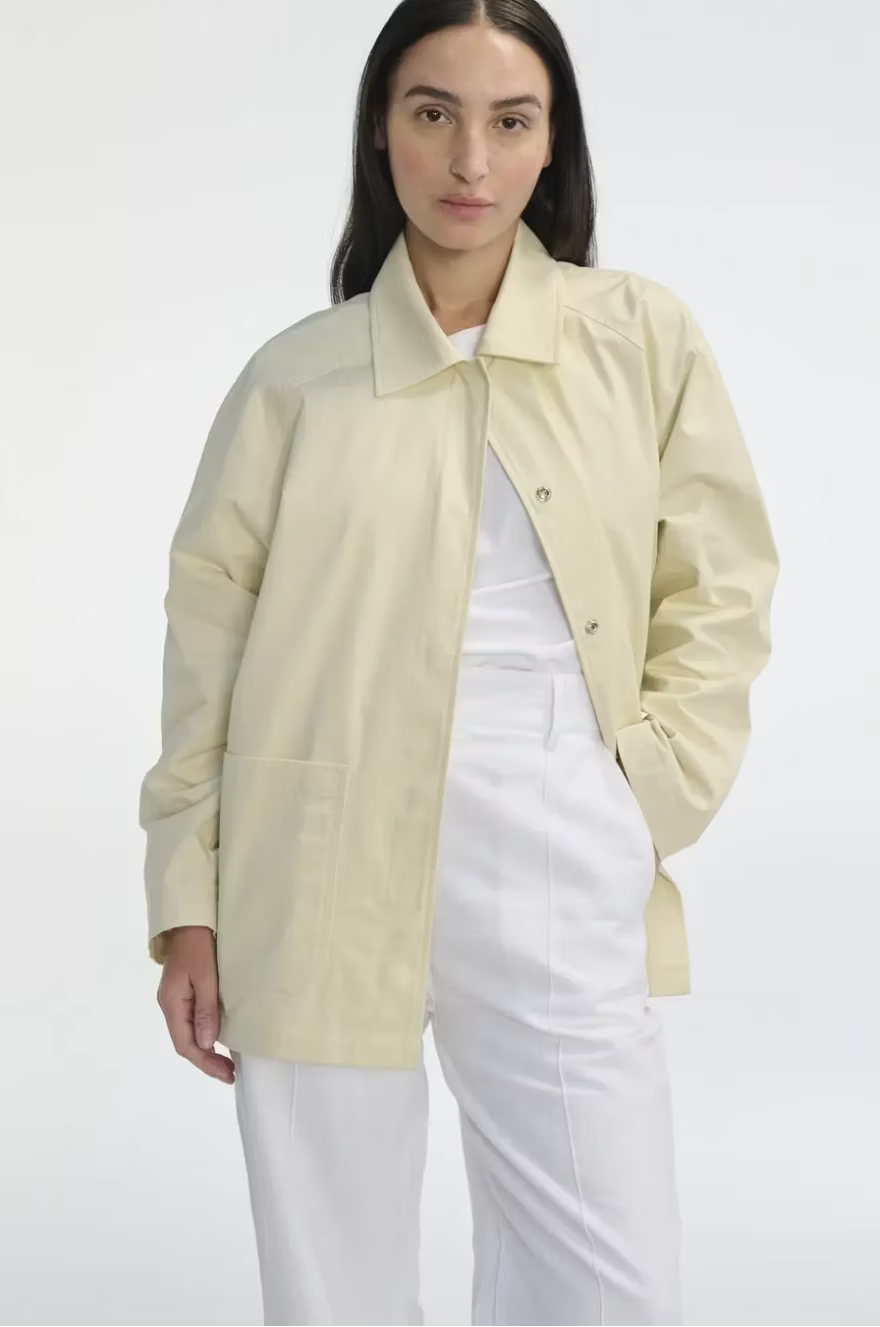 Woman wearing a light yellow jacket over a white outfit on a white background
